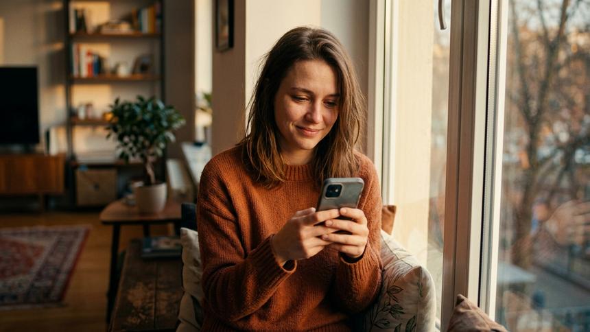 窓辺でくつろぎながらスマートフォンを操作する女性。