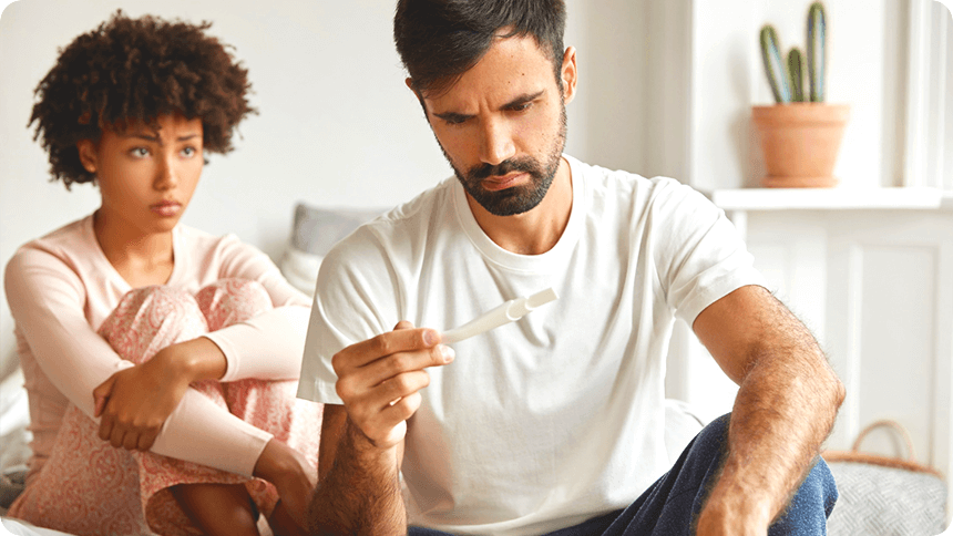 不安そうな彼女と、真剣な表情で妊娠検査薬を見つめる男性