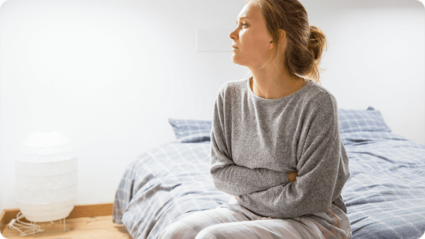 ベッドに座り、下腹部をぐっと両手で抱き込んでいる体調が悪そうな女性