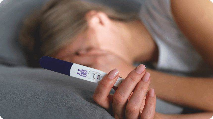 結果の出た妊娠検査薬を持ち、顔を片方の手で覆うようにしてベッドで横になっている女性