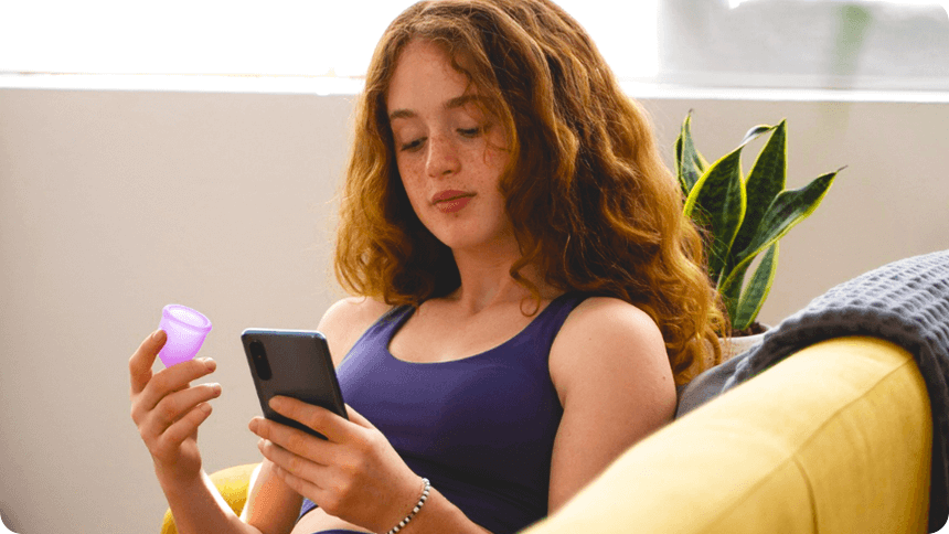 月経カップを持ちながらスマートフォンで何かを見ている女性