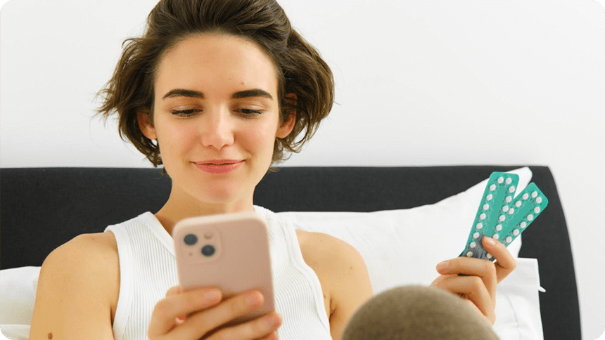 ピルを片手に、スマホで調べものをする女性