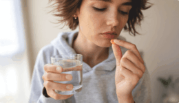 片手でコップを持ち、片手で口元へ薬を運ぶ女性