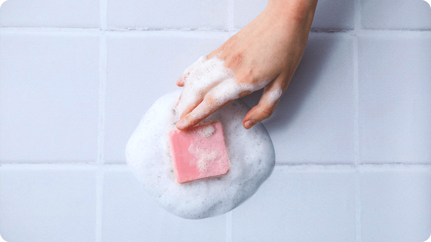 泡がついたタイルの上にあるピンクの石鹸に触れる手元