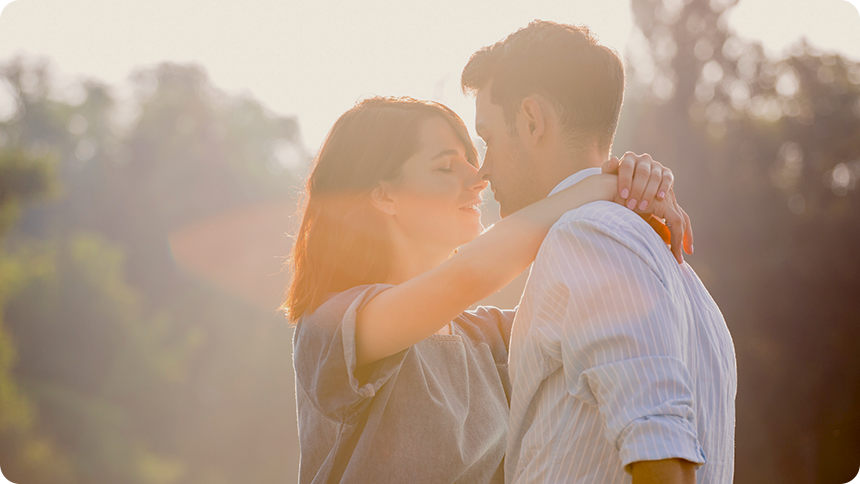 光の中で女性が男性の肩に両腕を回して今にも口付けをする瞬間