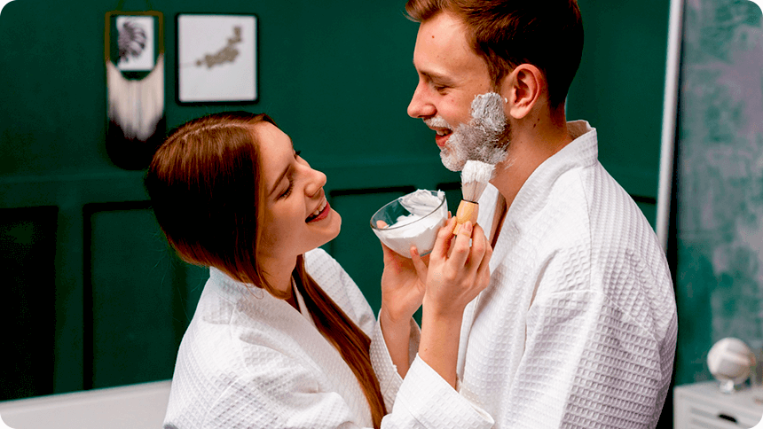 洗面所で、彼女が彼のフェイスラインにシェービングフォームを塗っている仲がよさそうな姿