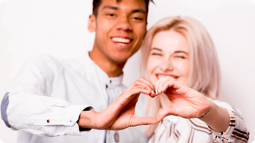 カップルが笑顔でハートのハンドサインを作っている
