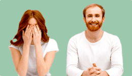 白い服を着たカップル。男性は笑顔でこちらを見ているのに対し、女性は机に肘をついて顔を手のひらで覆ている。