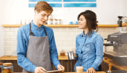 カフェで働く男女スタッフが笑顔で会話する様子。バイト先での自然なコミュニケーションを描いたシーン。