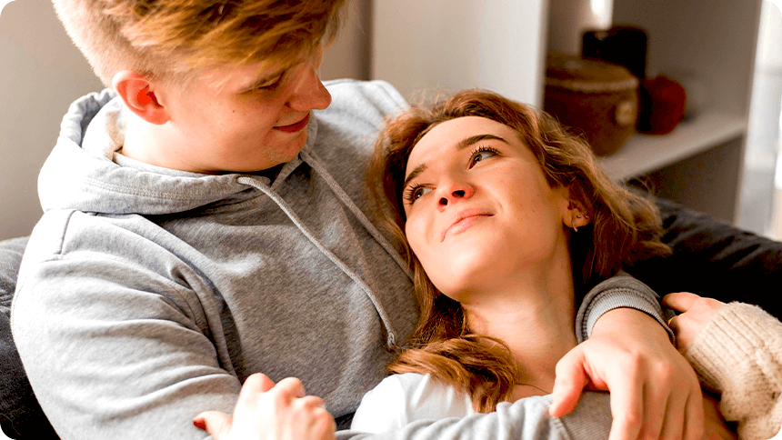 ソファで寄り添いながら見つめ合うカップル。穏やかで温かい愛情を感じさせる瞬間。