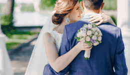 花嫁が新郎の肩に手を添えながら寄り添うシーン。ブーケを手にした幸福感のある後ろ姿