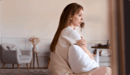 ベッドに座り、クッションを抱えて物思いにふける女性