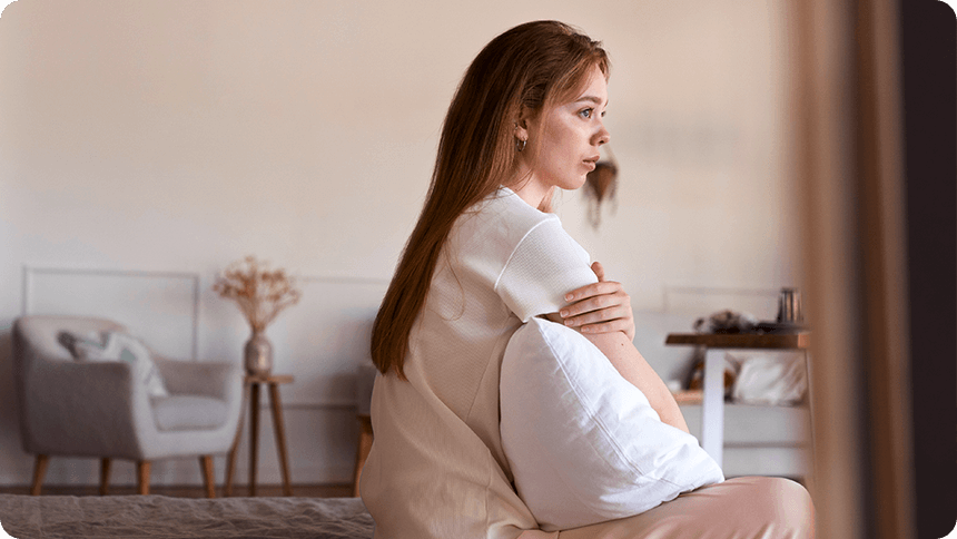 ベッドに座り、クッションを抱えて物思いにふける女性