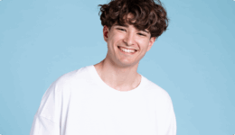 水色の背景の前で、白いTシャツを着て笑顔を見せる男性