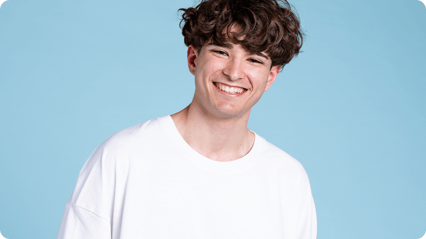 水色の背景の前で、白いTシャツを着て笑顔を見せる男性