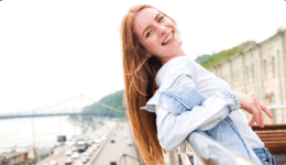 屋外の手すりにもたれ、振り返って笑う女性