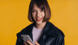 スマートフォンを片手に、明るくて優しい笑顔を携えてこちらを見つめる女性