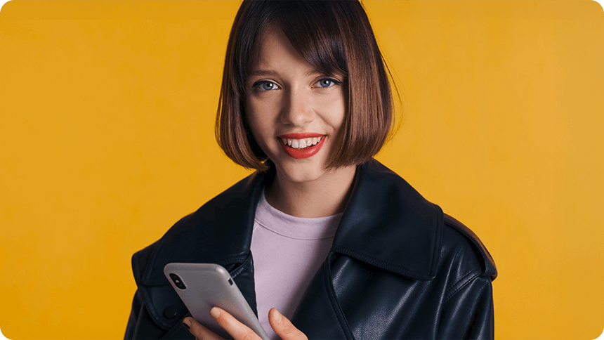 スマートフォンを片手に、明るくて優しい笑顔を携えてこちらを見つめる女性