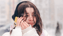 雪が降る屋外で、スマートフォンを耳に当てながら不安そうな表情を浮かべている女性。