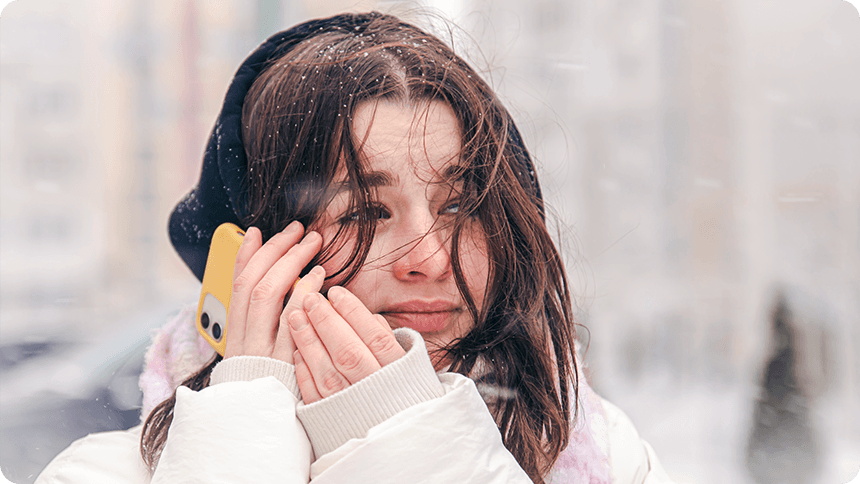 雪が降る屋外で、スマートフォンを耳に当てながら不安そうな表情を浮かべている女性。