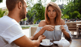 カフェで向かい合う男女。女性がどこか不満そうな表情を浮かべながら話を聞いており、二人の間に微妙な距離感が感じられる様子。