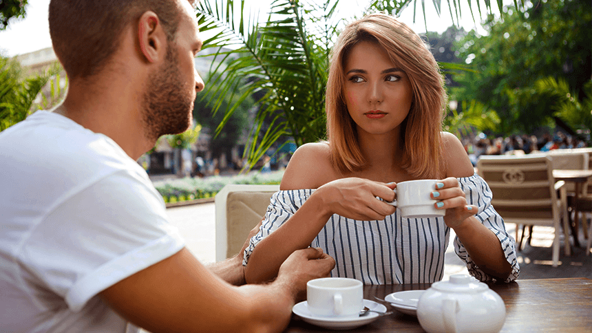 カフェで向かい合う男女。女性がどこか不満そうな表情を浮かべながら話を聞いており、二人の間に微妙な距離感が感じられる様子。