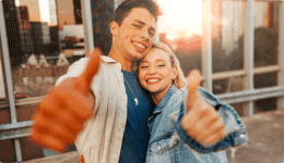 夕暮れの街で、笑顔のカップルが親指を立ててポーズをする楽しげな様子