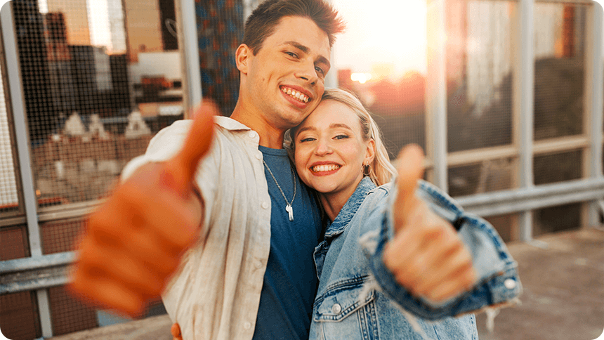 夕暮れの街で、笑顔のカップルが親指を立ててポーズをする楽しげな様子