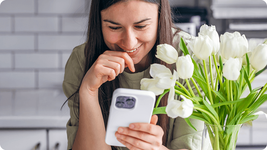 白い花のそばでスマートフォンを見つめる女性