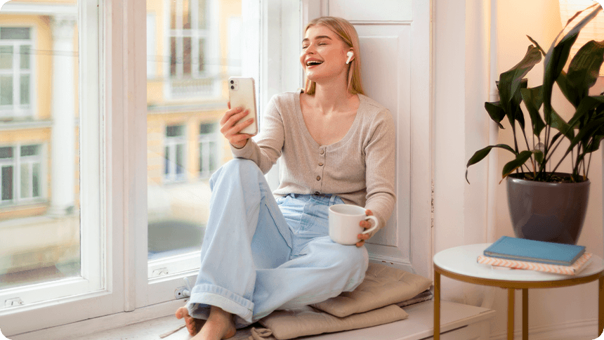 窓辺のリラックスした空間で、笑顔でスマホを見つめる女性