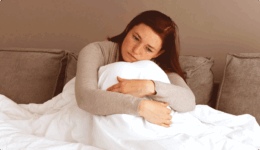 ベッドで膝にかかった布団ごと膝を抱える女性