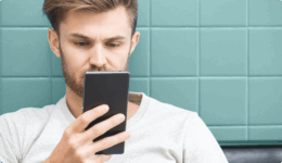 カフェ風の壁を背にスマホ画面を真剣に見つめる男性