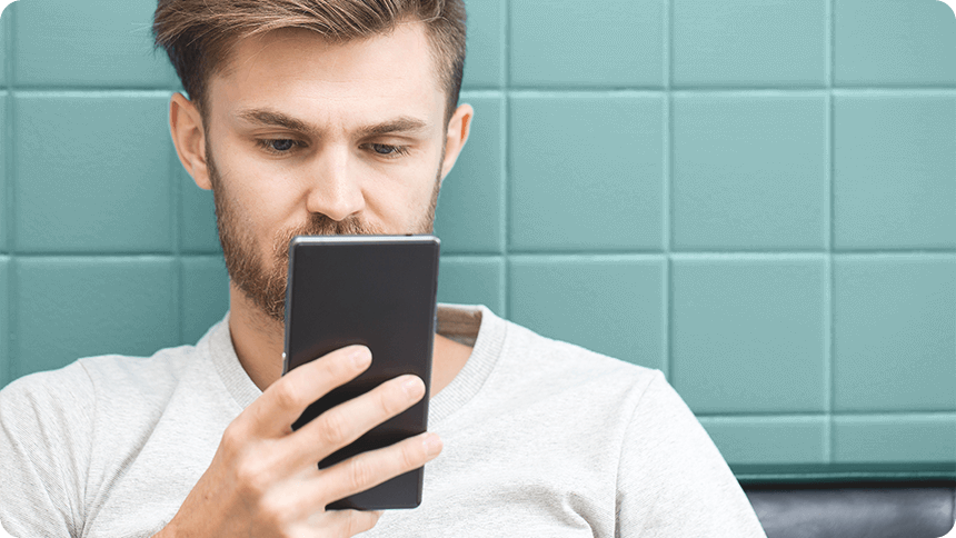 カフェ風の壁を背にスマホ画面を真剣に見つめる男性