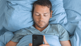 布団に包まりながらスマホを見ているリラックスした男性