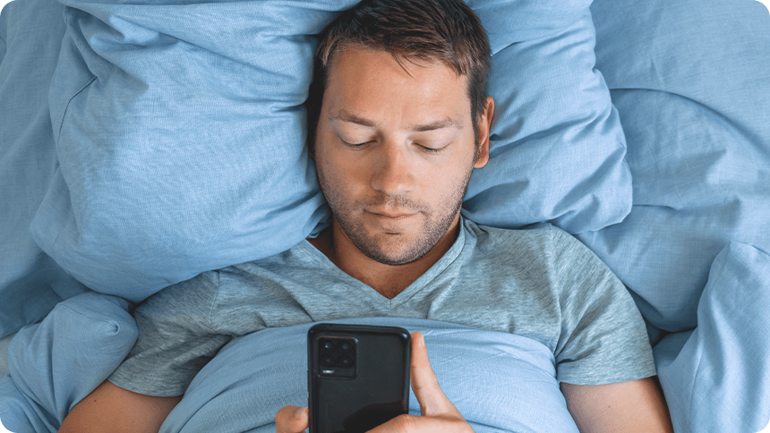 布団に包まりながらスマホを見ているリラックスした男性