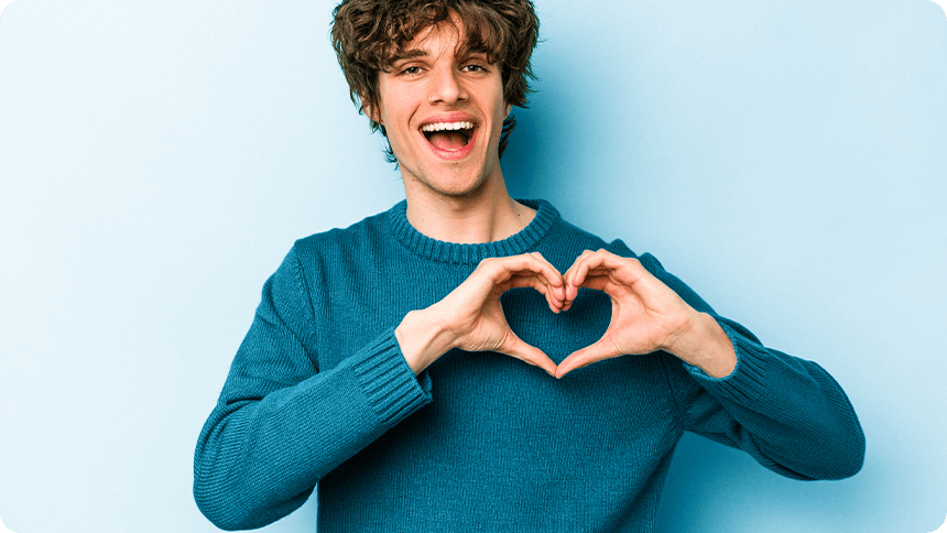 青い背景の前で手でハートを作り笑顔を見せる男性