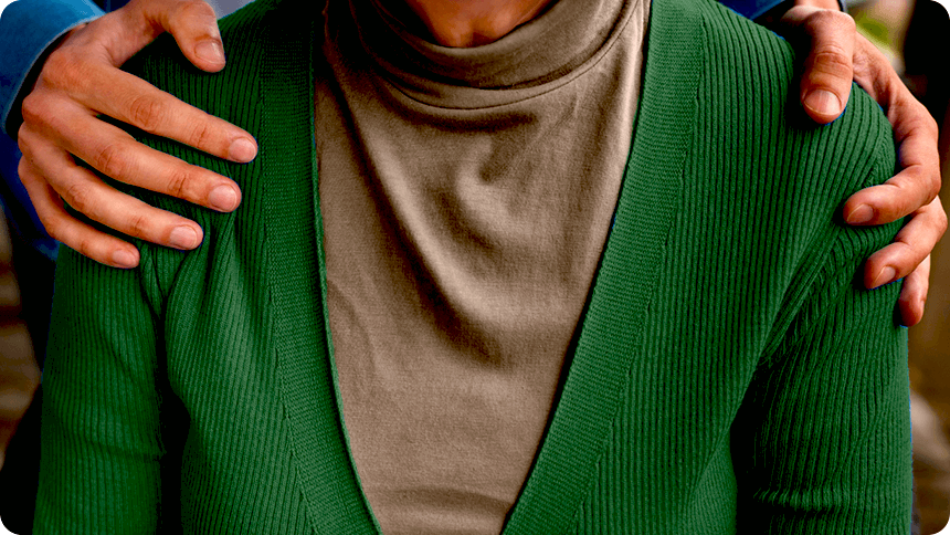 背後から、座っている女性の肩に手を置く男性の手元