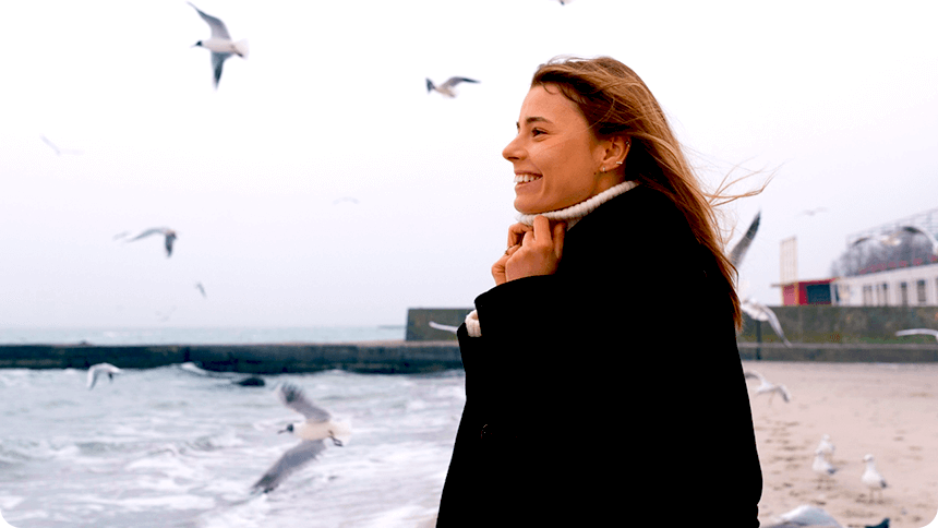 海岸沿いでカモメが空を飛び回るのを笑顔で見る女性