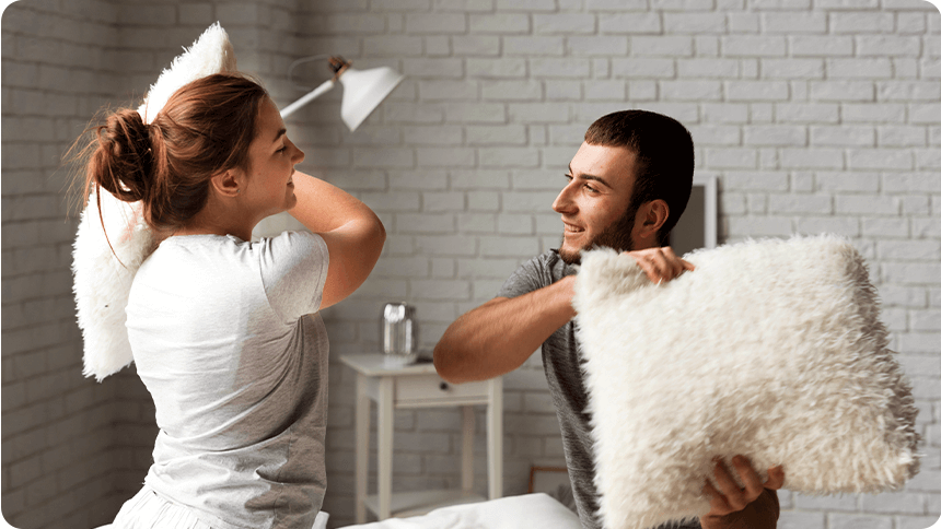 部屋の中で枕投げを楽しむカップル。リラックスした雰囲気の中でじゃれ合う様子