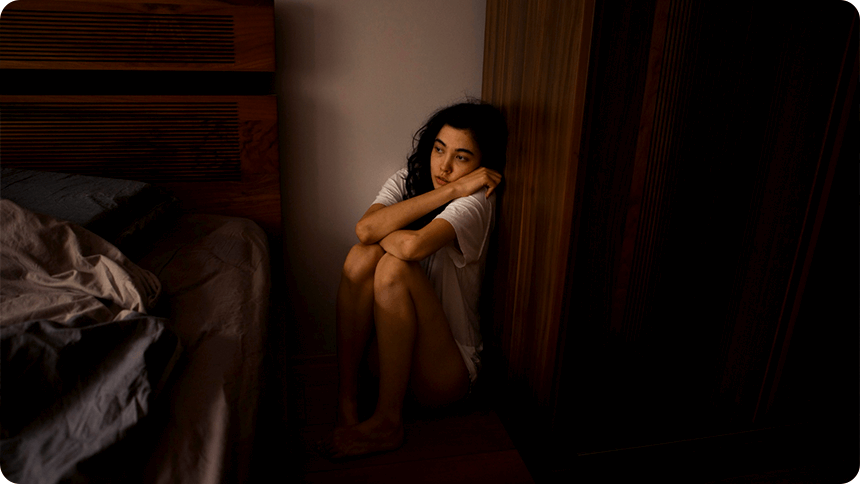暗い部屋で、ベッドト壁の隙間に座り込む女性