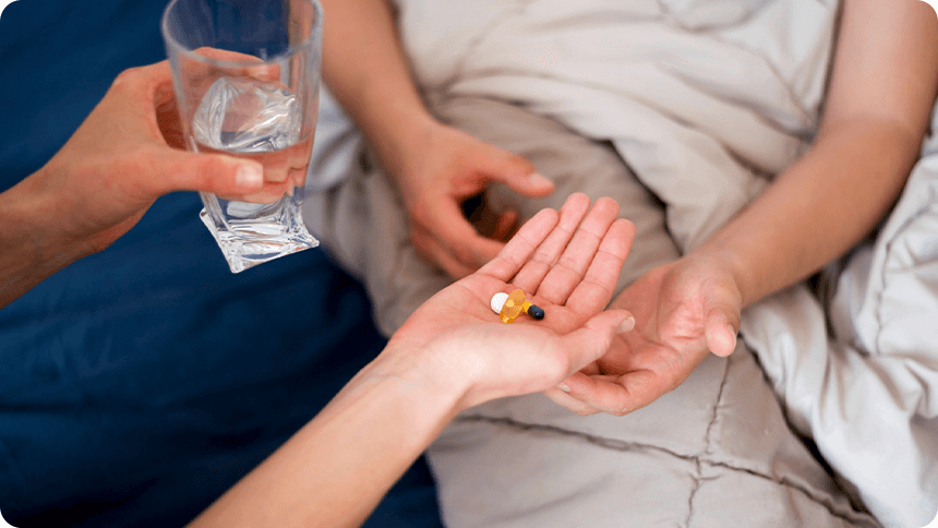 彼がベッドにいる彼女へ薬と水を渡す手元