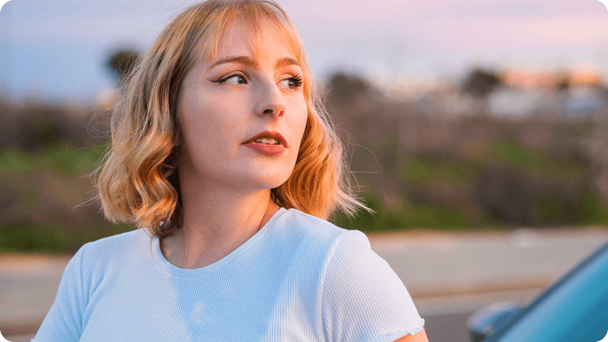 夕暮れの屋外で横を向いて遠くを見つめるブロンドの女性