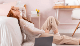 明るい部屋の中でベッドにもたれ額に手を当てて悩んでいる様子の女性