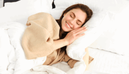 清潔な白い布団に包まれ、心地よい表情で眠る女性。夢の中で起こる体の自然な反応や、心身のメンテナンスを象徴する、安心感と健やかさに満ちた睡眠のひととき。