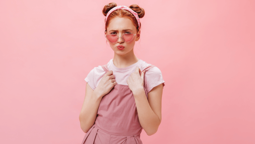 ピンクの背景の前で、頬をふくらませながらこちらを見つめる女性